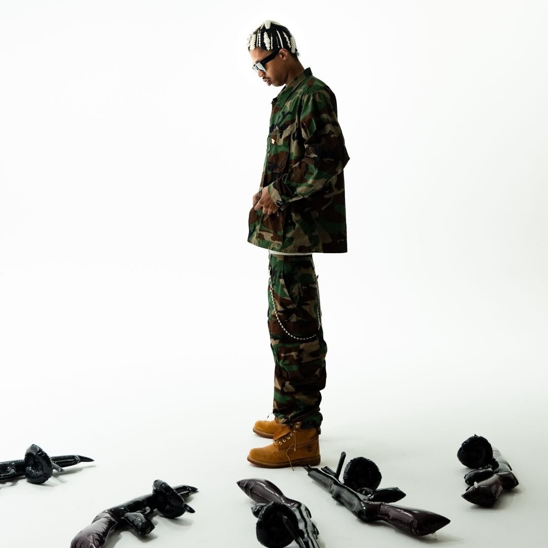 Thoto in camo standing among inflatable guns on white